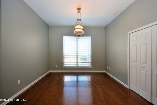 spare room with dark hardwood / wood-style floors and an inviting chandelier