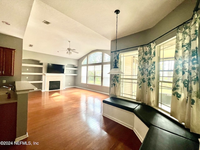 living room with ceiling fan, hardwood / wood-style floors, a textured ceiling, lofted ceiling, and a tiled fireplace