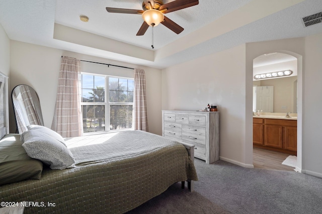 bedroom featuring light carpet, sink, ensuite bathroom, ceiling fan, and a raised ceiling