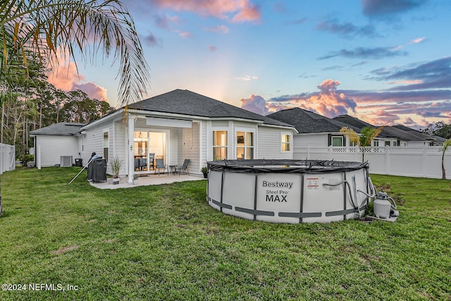 back house at dusk featuring central AC unit, a patio area, a yard, and a covered pool