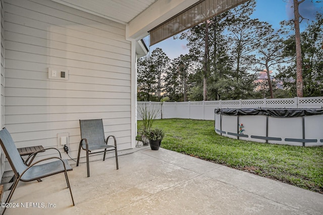 patio terrace at dusk featuring a lawn and a covered pool