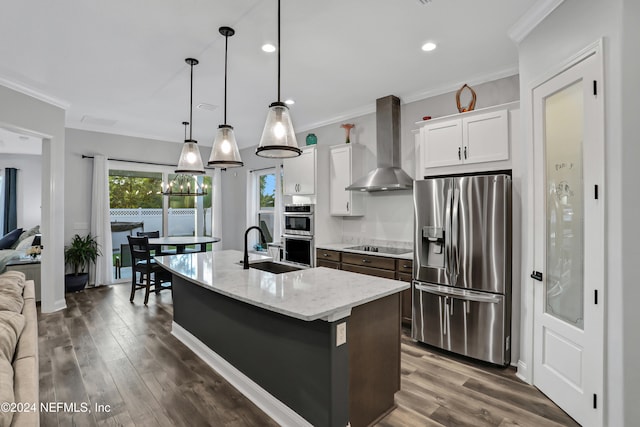 kitchen featuring stainless steel appliances, wall chimney exhaust hood, white cabinetry, and a center island with sink