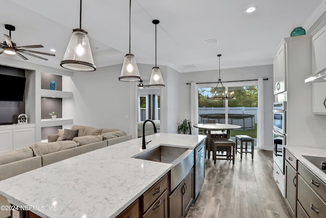 kitchen featuring white cabinetry, light wood-type flooring, decorative light fixtures, and an island with sink