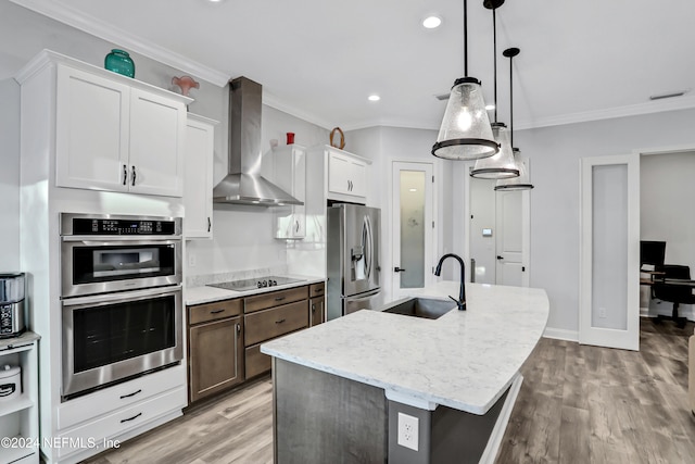 kitchen with a center island with sink, white cabinets, wall chimney exhaust hood, sink, and appliances with stainless steel finishes