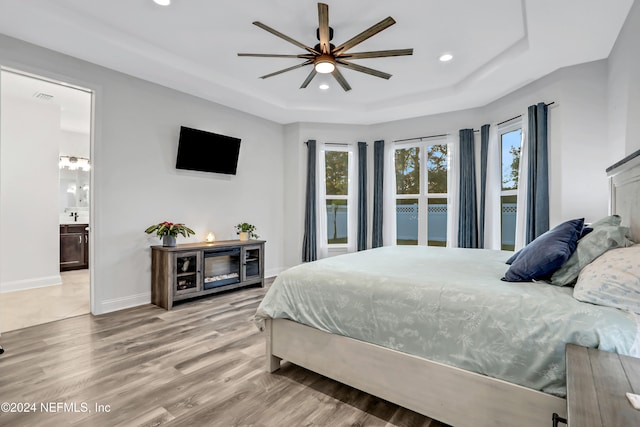 bedroom featuring connected bathroom, a tray ceiling, hardwood / wood-style floors, and ceiling fan