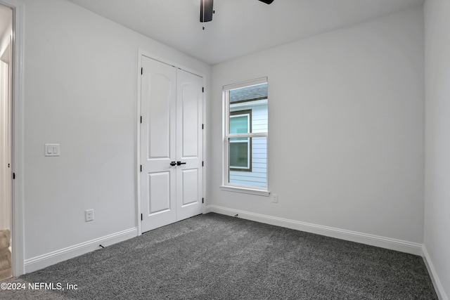 unfurnished bedroom with ceiling fan, a closet, and dark carpet