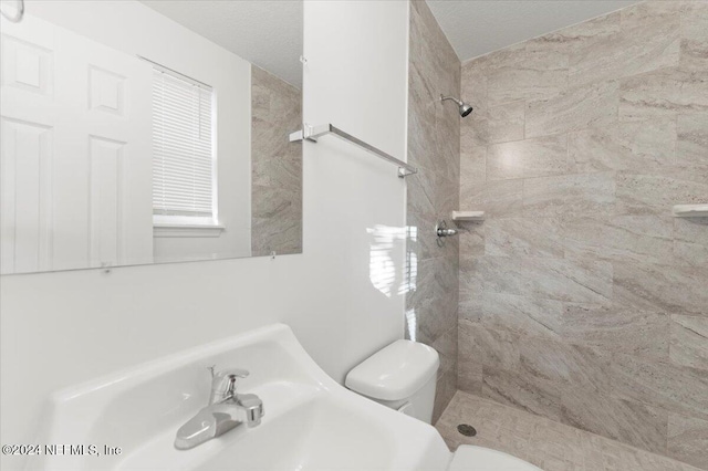 bathroom with a tile shower, sink, a textured ceiling, and toilet