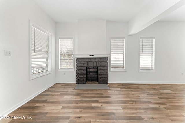 unfurnished living room featuring wood-type flooring and a brick fireplace