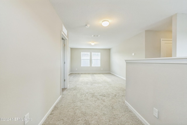 unfurnished room featuring baseboards, a textured ceiling, visible vents, and light colored carpet