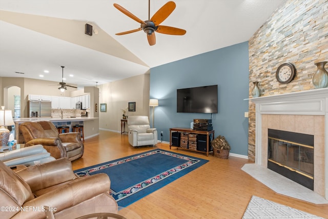 living room featuring a fireplace, light hardwood / wood-style floors, ceiling fan, and vaulted ceiling