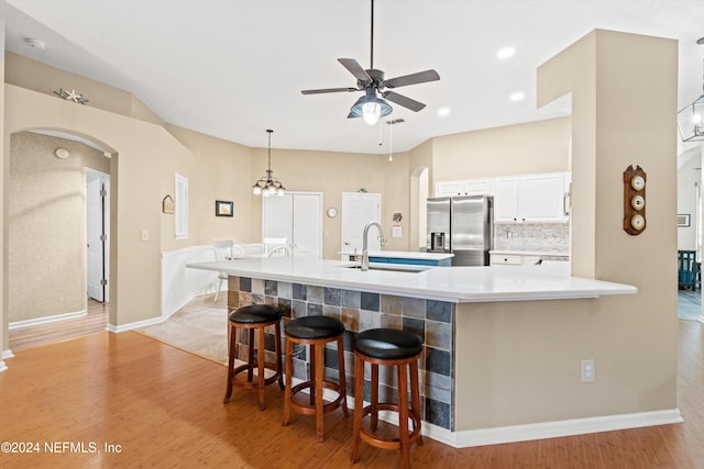 kitchen featuring white cabinets, a kitchen bar, stainless steel fridge with ice dispenser, and light hardwood / wood-style flooring