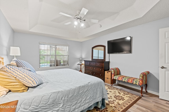 bedroom with a tray ceiling, ceiling fan, and light hardwood / wood-style flooring