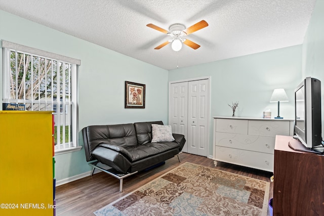 living room featuring dark wood-type flooring, a textured ceiling, and ceiling fan