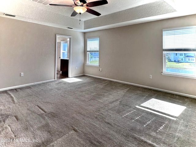 unfurnished room with a raised ceiling, ceiling fan, dark carpet, and a textured ceiling