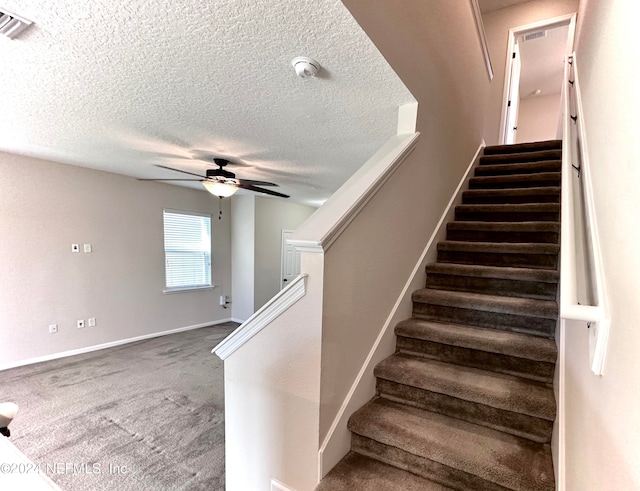 staircase with a textured ceiling, ceiling fan, and carpet flooring