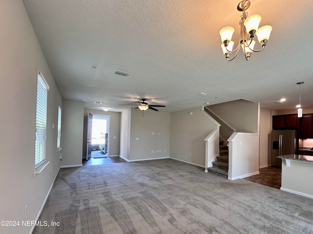 unfurnished living room featuring ceiling fan with notable chandelier, a textured ceiling, and dark carpet