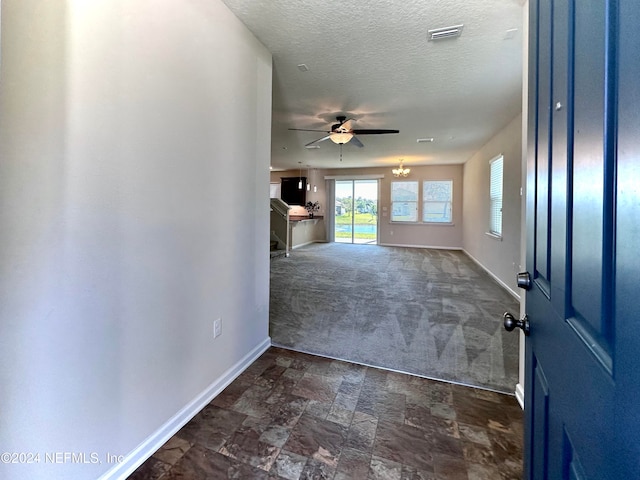 unfurnished living room with ceiling fan, dark carpet, and a textured ceiling