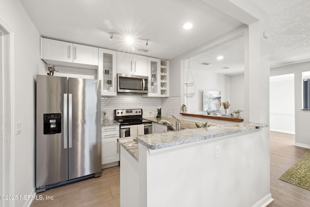 kitchen with kitchen peninsula, white cabinetry, stainless steel appliances, and light stone counters