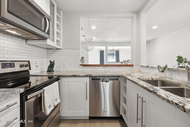 kitchen featuring light stone countertops, appliances with stainless steel finishes, tasteful backsplash, sink, and white cabinetry