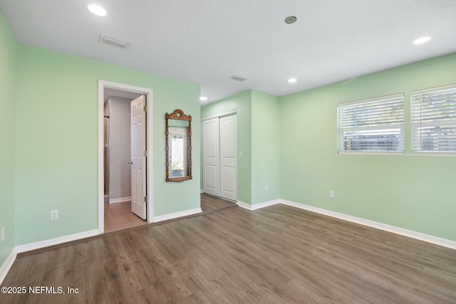 unfurnished bedroom featuring a textured ceiling, ensuite bath, dark wood-type flooring, and a closet