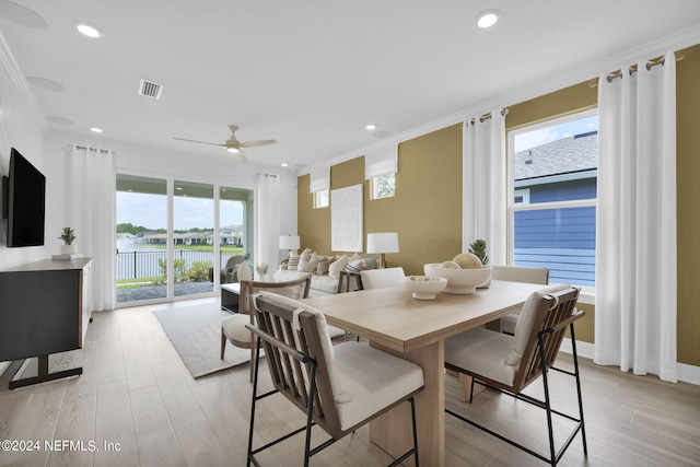 dining room featuring ornamental molding, light hardwood / wood-style flooring, a water view, and ceiling fan