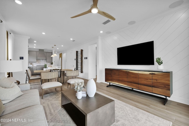 living room featuring ceiling fan, light wood-type flooring, and crown molding