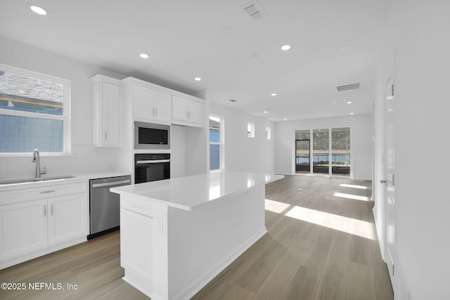 kitchen with stainless steel appliances, a sink, white cabinetry, visible vents, and light wood-style floors