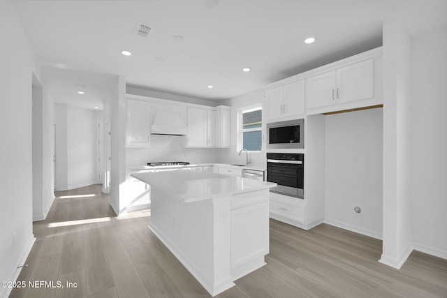 kitchen with light wood finished floors, appliances with stainless steel finishes, white cabinetry, and custom range hood