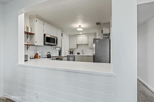 kitchen featuring decorative backsplash, kitchen peninsula, stainless steel appliances, sink, and white cabinets