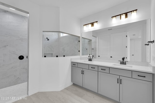 bathroom with wood finished floors, double vanity, a sink, and walk in shower