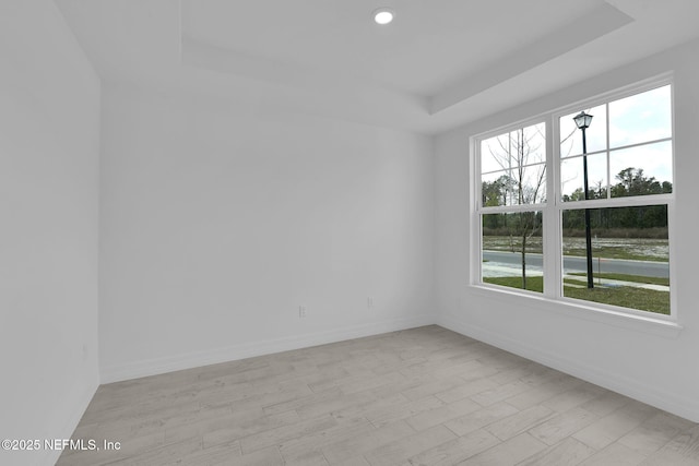 spare room featuring a tray ceiling, light wood-style flooring, baseboards, and recessed lighting