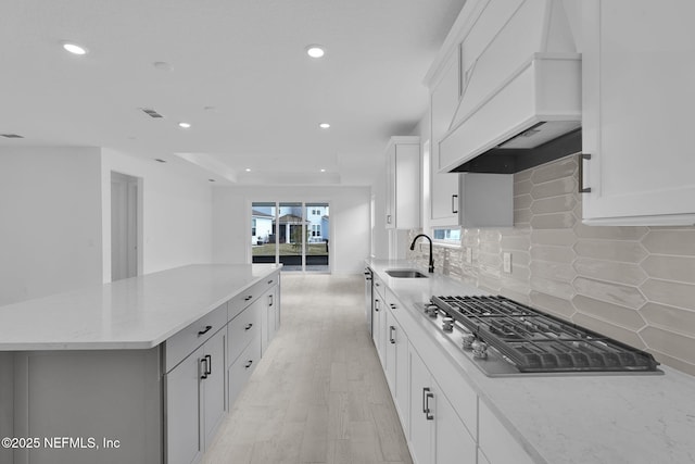 kitchen featuring a kitchen island, custom exhaust hood, stainless steel gas cooktop, a sink, and recessed lighting