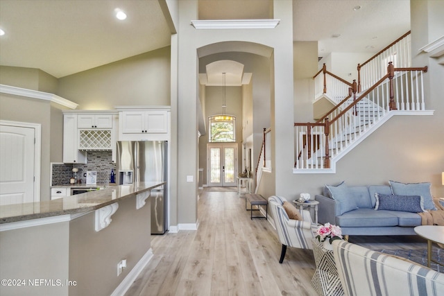 kitchen with backsplash, high vaulted ceiling, white cabinets, light hardwood / wood-style flooring, and light stone countertops