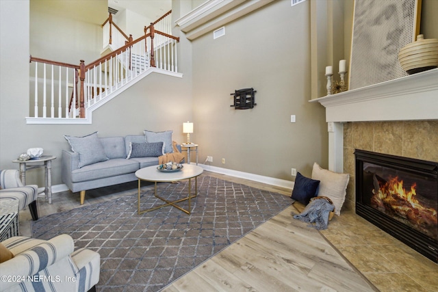 living room with a tiled fireplace, hardwood / wood-style floors, and a high ceiling