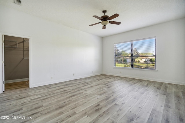 unfurnished bedroom with a spacious closet, ceiling fan, light hardwood / wood-style flooring, a textured ceiling, and a closet