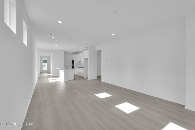 unfurnished living room with recessed lighting, a sink, light wood-style flooring, and baseboards