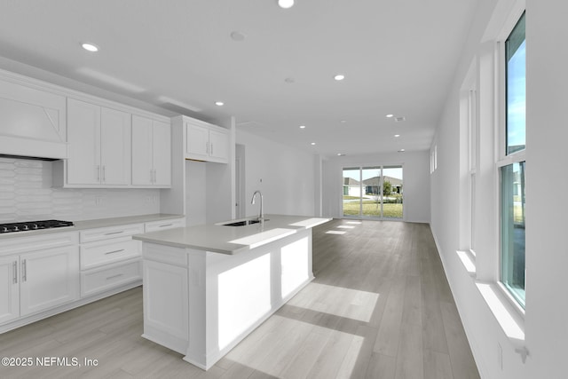 kitchen featuring black stovetop, decorative backsplash, light wood-style floors, white cabinets, and a sink