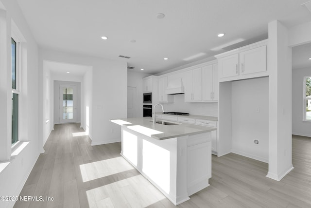 kitchen featuring visible vents, white cabinets, light wood finished floors, a center island with sink, and custom range hood