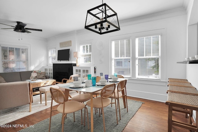 dining area with ceiling fan, wood-type flooring, ornamental molding, and a brick fireplace