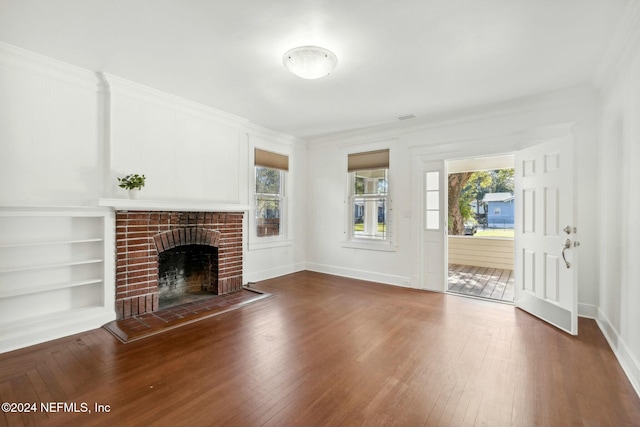 unfurnished living room featuring a brick fireplace, crown molding, built in features, and hardwood / wood-style flooring