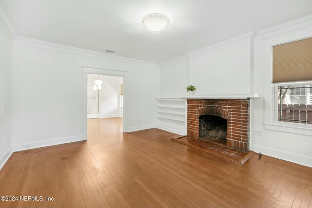 unfurnished living room with hardwood / wood-style floors, a brick fireplace, and ornamental molding