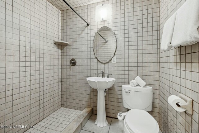 bathroom with a tile shower, tile patterned floors, tile walls, and toilet