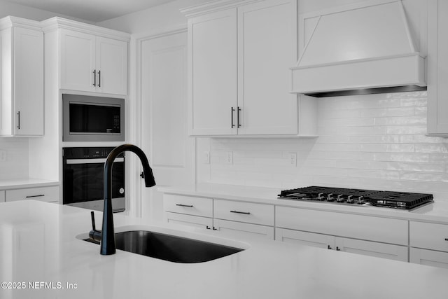 kitchen featuring wall oven, built in microwave, premium range hood, stainless steel gas stovetop, and a sink