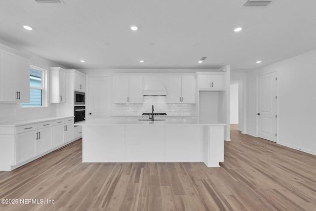 kitchen with a kitchen island with sink, a sink, black oven, light countertops, and stainless steel microwave