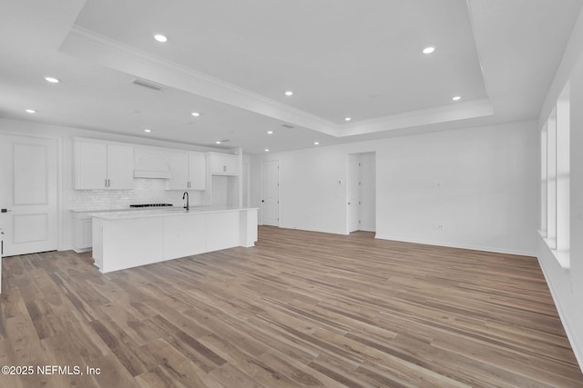 unfurnished living room featuring light wood-type flooring, a raised ceiling, crown molding, and recessed lighting