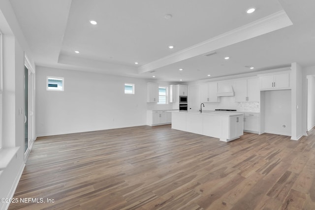 kitchen with light wood-style flooring, a sink, open floor plan, a tray ceiling, and custom range hood