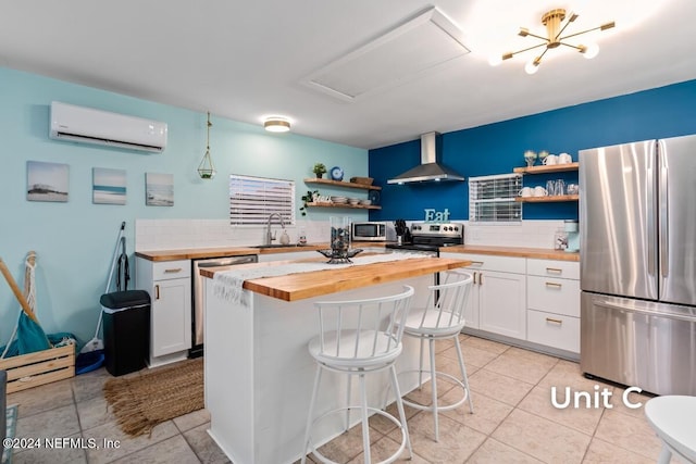 kitchen with wall chimney range hood, appliances with stainless steel finishes, white cabinetry, wood counters, and an AC wall unit