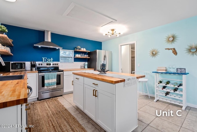 kitchen with white cabinetry, wall chimney range hood, stainless steel appliances, and wooden counters