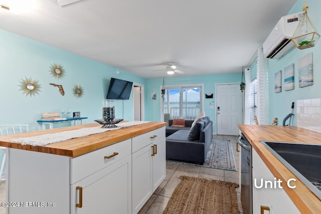 kitchen featuring an AC wall unit, white cabinets, wooden counters, stainless steel dishwasher, and ceiling fan