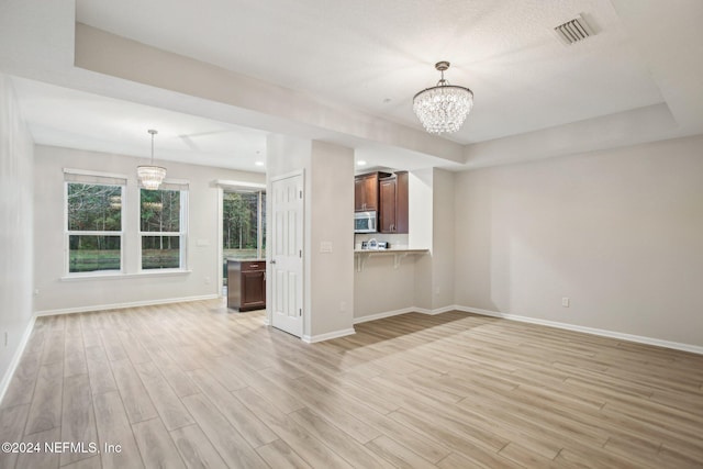 unfurnished living room with a raised ceiling, light hardwood / wood-style flooring, and an inviting chandelier